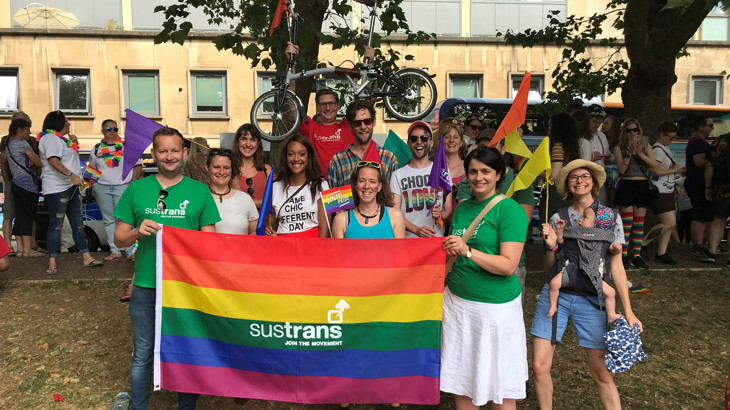 A group of Walk Wheel Cycle Trust colleagues and friends marching at the 2018 Pride March in Bristol, holding a Walk Wheel Cycle Trust flag.