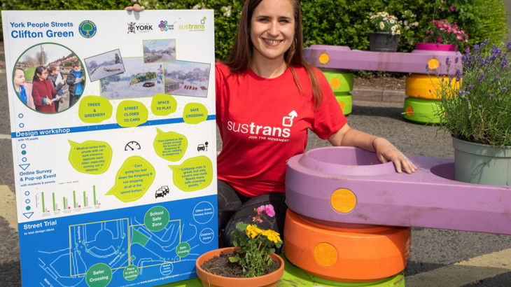 woman out on the street with flower pot and sign explaining the trial
