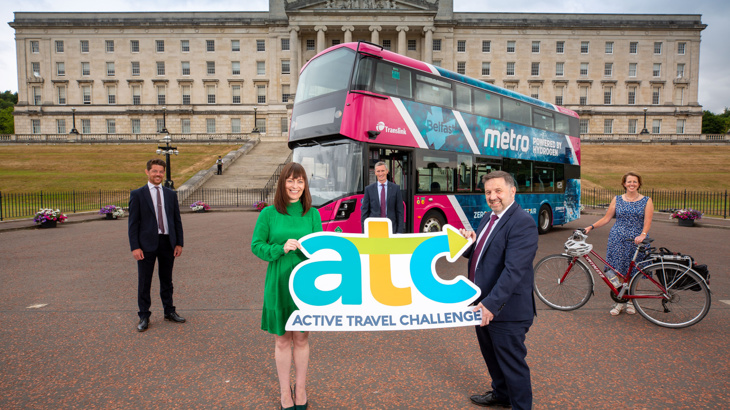 Active Travel Launch in front of Stormont Buildings with Infrastructure Minister Nichola Mallon and Health Minister Robin Swan holding a large ATC cutout, David Tumility Public Health Agency, Chris Conway Translink and Caroline Bloomfield, Walk Wheel Cycle Trust pictured in the background with a bus and bicycle