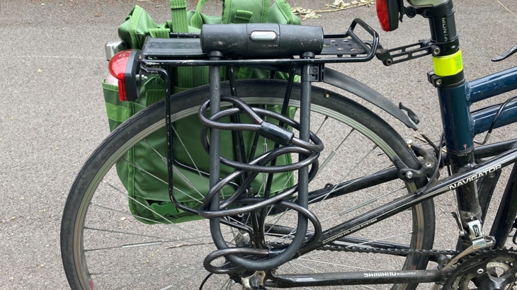 Lock hanging from pannier rack with cable woven through it.