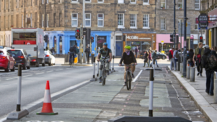 Two people cycle within a separated cycle way on a busy road as part of Spaces for People measures in Edinburgh city centre.