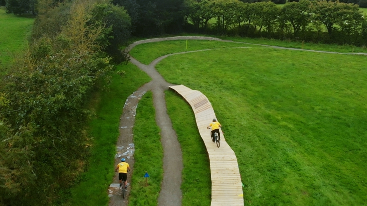 two people cycling on cycle track, surrounded by greenery