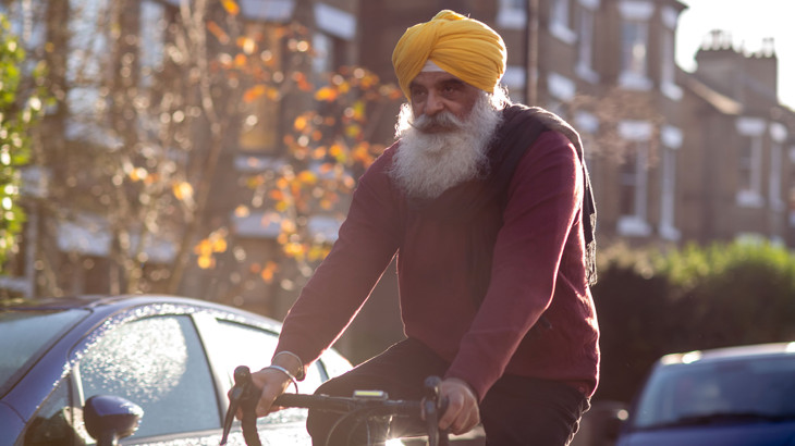 Older Sikh man cycling down a road