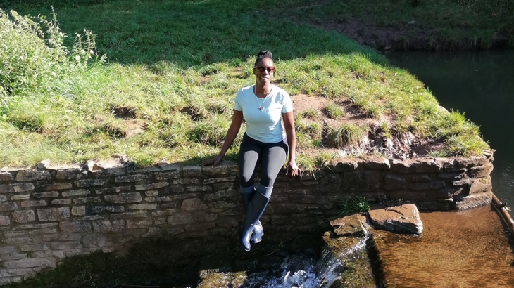 Sophie Brown of Steppin Sistas sits on a wall beside a watercourse in the countryside.