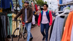 Two people stroll through a London market, one pushing a bike.