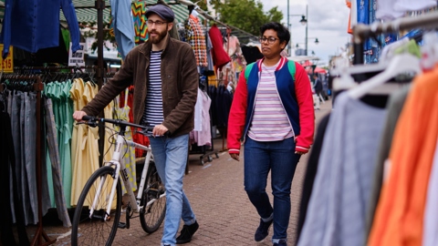 Two people stroll through a London market, one pushing a bike.
