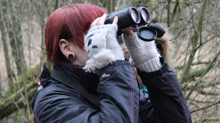 A volunteer raises a set of binoculars to their face during a bird identification session along a traffic-free route of the National Cycle Network.