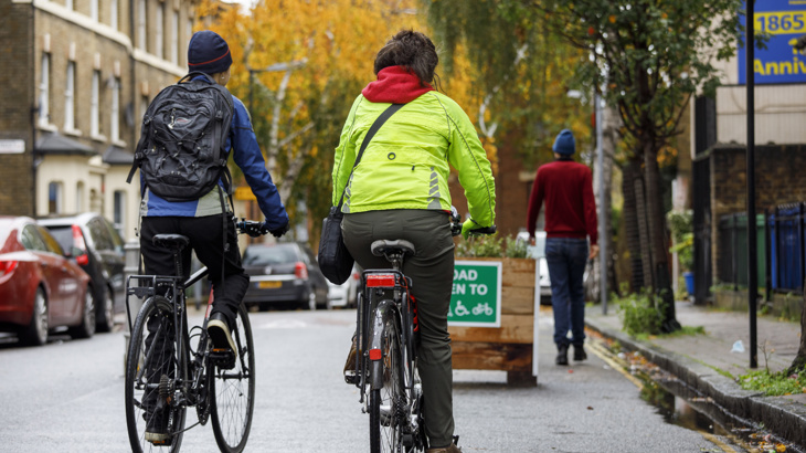 Two people on bikes wearing winter coats cycle in a low traffic neighbourhood in London.