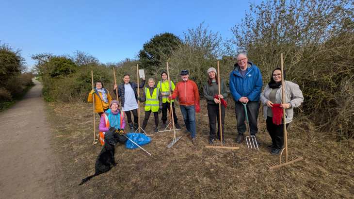 A group of volunteers on the National Cycle Network holding rakes, smiling into the camera, ready to start planting wildflowers.