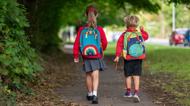 A brother and sister walking along a pavement to school.