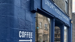 The blue shopfront of Unorthodox Roasters with the word 'Coffee' painted on it and an arrow pointing to the entrance.