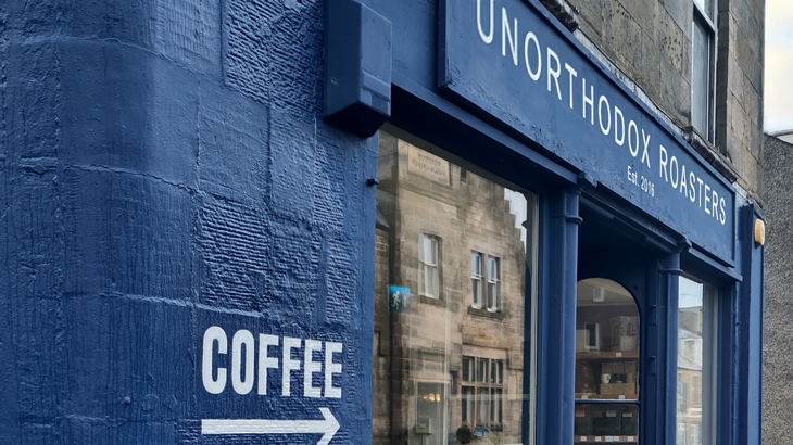 The blue shopfront of Unorthodox Roasters with the word 'Coffee' painted on it and an arrow pointing to the entrance.