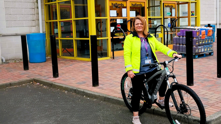 Woman wearing hi-vis sitting on new bike outside a bike shop