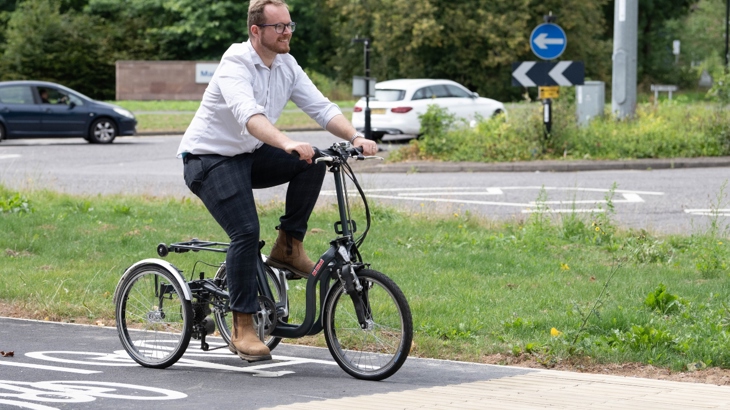 A man rides a tricycle on a cycle lane beside a road