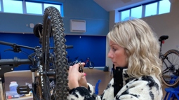 An adult woman practising bike maintenance on a bike in a maintenance stand.