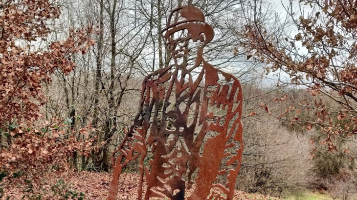 A steel sculpture of a man with glasses and a moustache wearing a bowler hat and carrying an umbrella surrounded by winter trees.