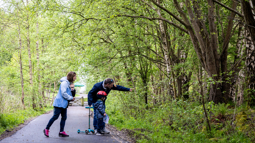 A family walking on the greenway pointing and looking into the forest, surrounded by green trees and shrubs.