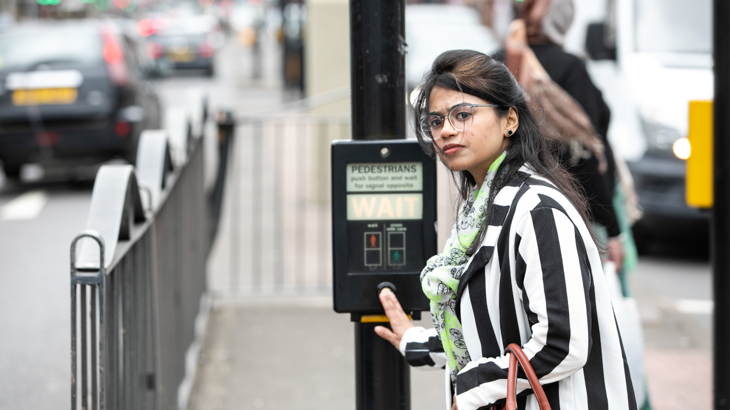 A person pressing the traffic light, looking onto the road to cross.