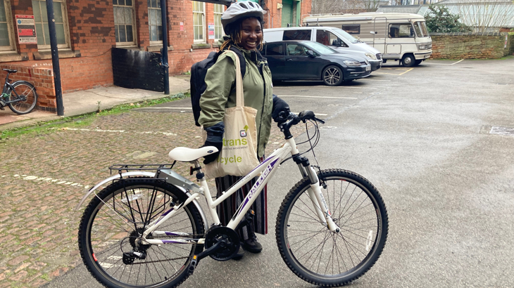 A person wearing a helmet, bag pack and tote bag standing in front of houses with their bike.