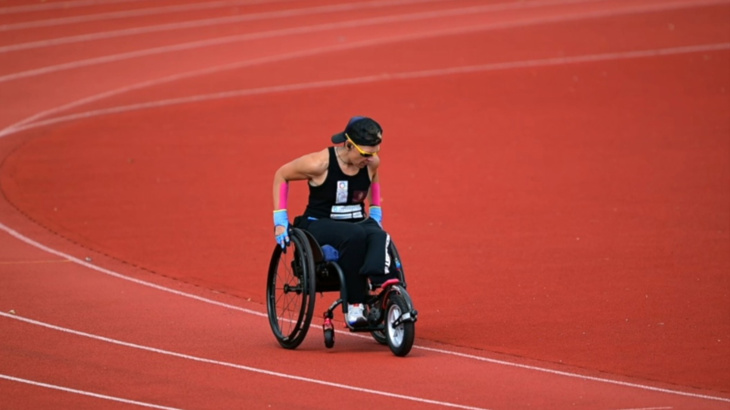 A woman wheeling on an outdoor track wearing sunglasses and a backwards cap