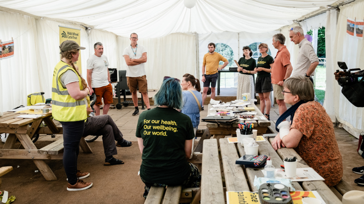 Walk Wheel Cycle Trust staff and volunteers gathered, chatting inside a tent with community activities and benches inside the tent.