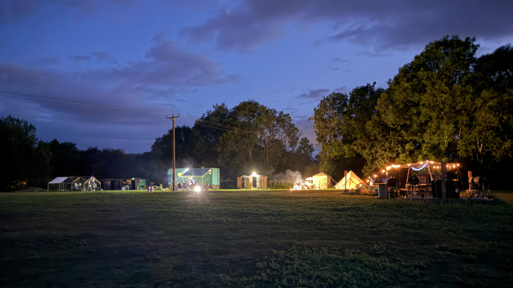 A campsite just after sunset, with lights on in the tents.