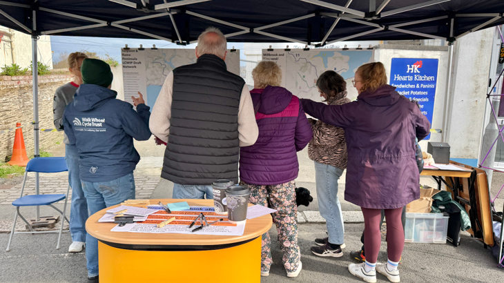 A group of people standing in front, looking at a proposed map of cycling and walking infrastructure in the area