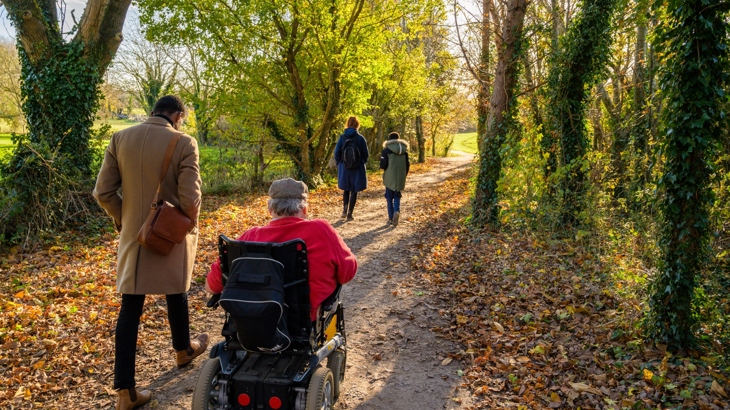 A group of people on a path, the festival way on a sunny autumn day. 3 people are walking and one person is wheeling.