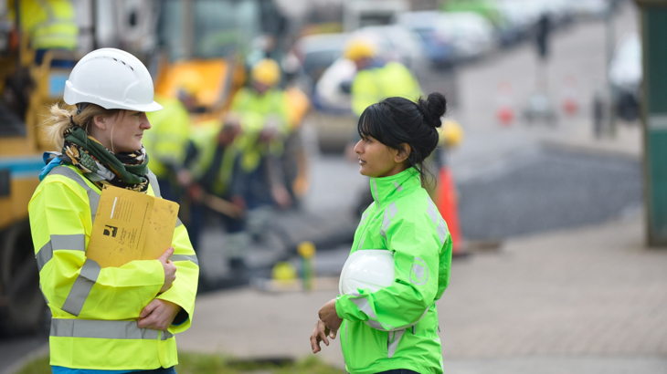 Two engineers in high vis and helmets standing on an infrastructure building site talking to each other