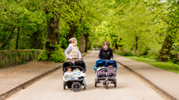 Two women pushing double buggies walking on traffic-free path by river in Cork.