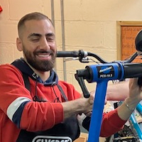 A man with a beard and short hair in a red hoodie stood smiling while fixing a mounted bike