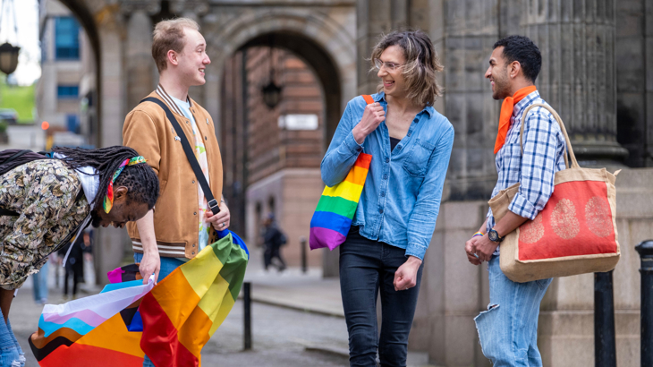 A group of people of mixed ethnicities holding and wearing rainbow pride bags and flags in Glasgow city centre