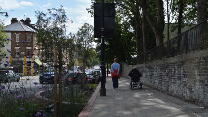 Two people, one in a wheelchair, on a pavement beside a busy road