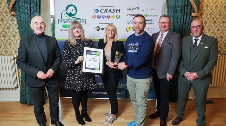 Two women and four men pose for a picture with a trophy and certificate.